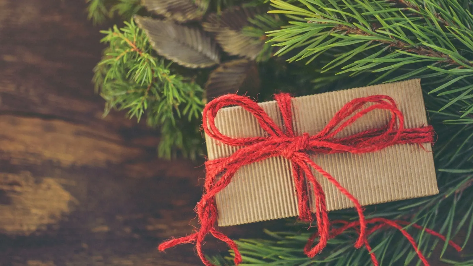 A kraft-paper gift tied with red twine on fir branches